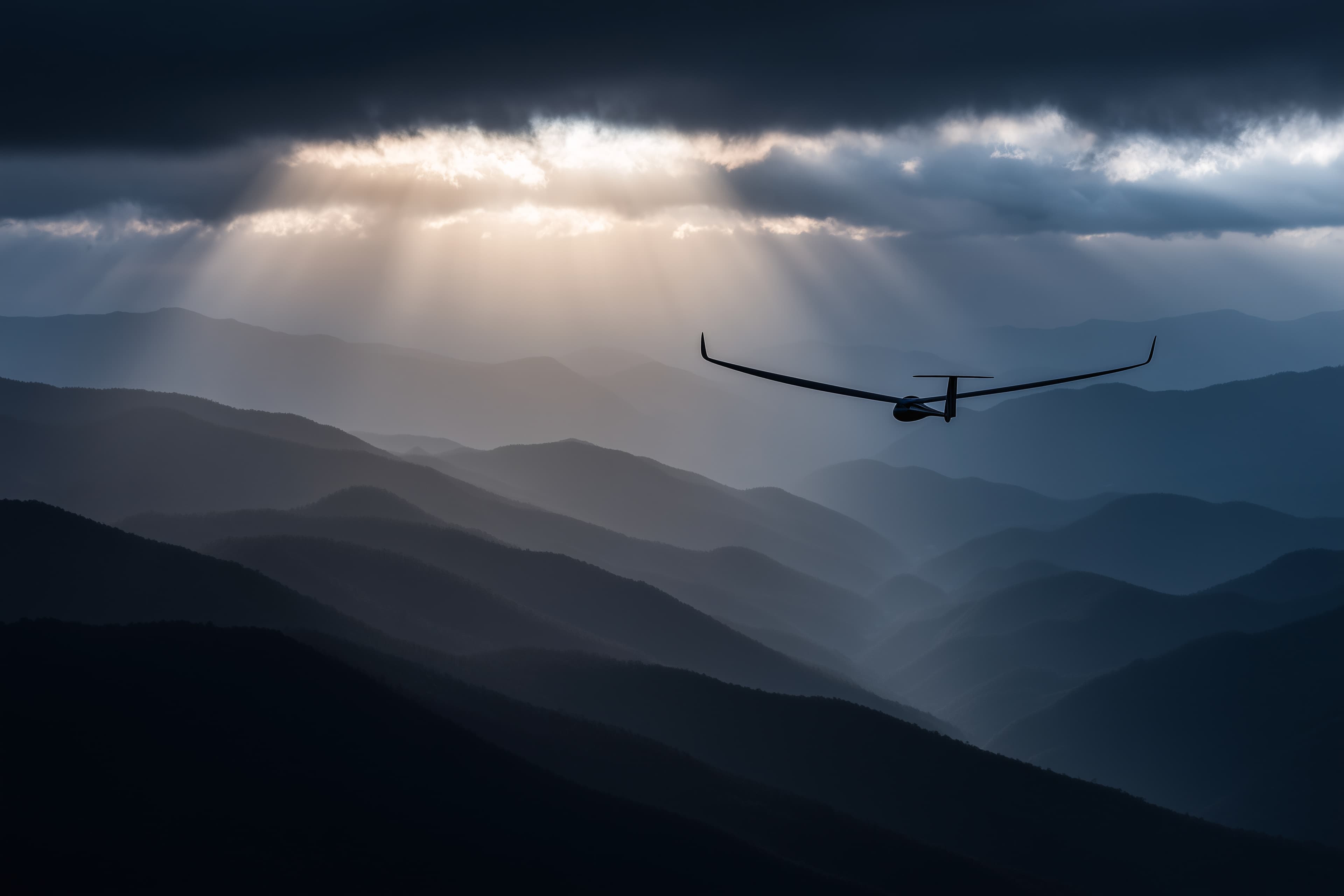 Glider soaring over mountain ridges with dramatic clouds and light rays